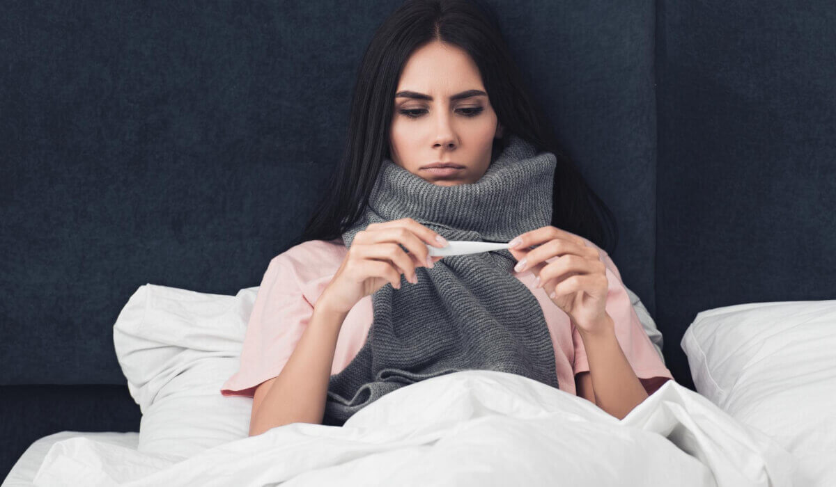 Krankgeschriebene Frau überprüft ihre Temperatur im Bett-DE