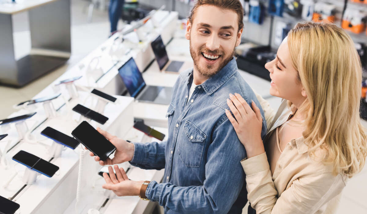 Lächelndes Paar auf der Suche nach einem Telefon und einem Laptop, die in einem Geschäft gekauft werden sollen