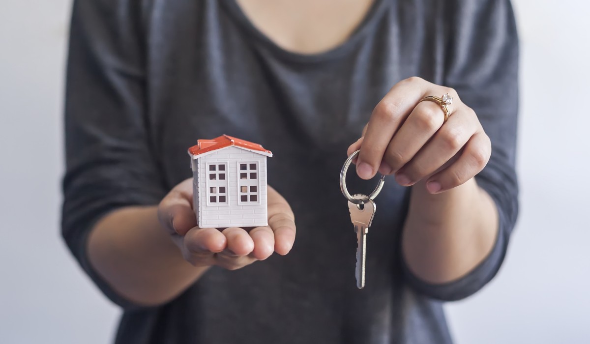 Жінка тримає в руках маленький будиночок і ключі