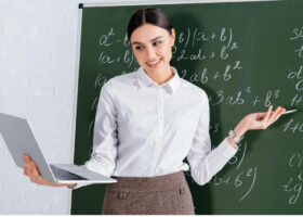 Ein Lehrer schreibt am Teacher's Day mit einem Laptop an die Tafel-DE