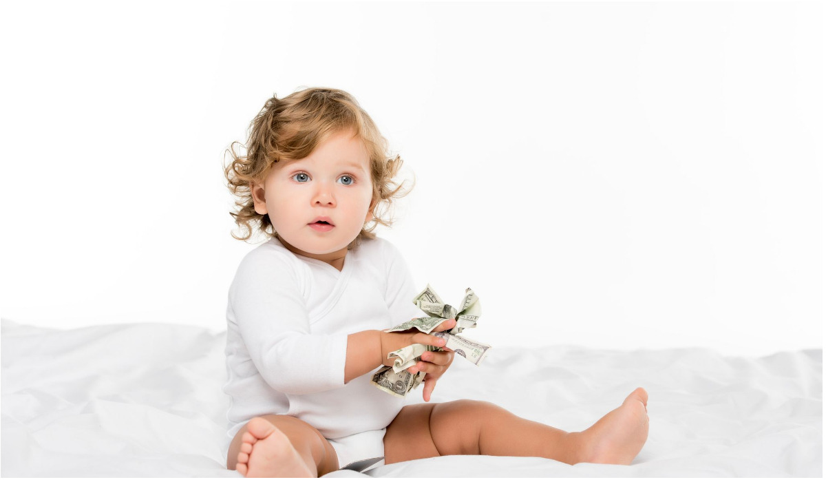 Ein Baby sitzt auf einem Bett mit Geld in den Händen-DE