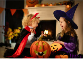 Девочки, одетые в костюмы, на праздник Хэллоуин в Германии сидят у камина-RU