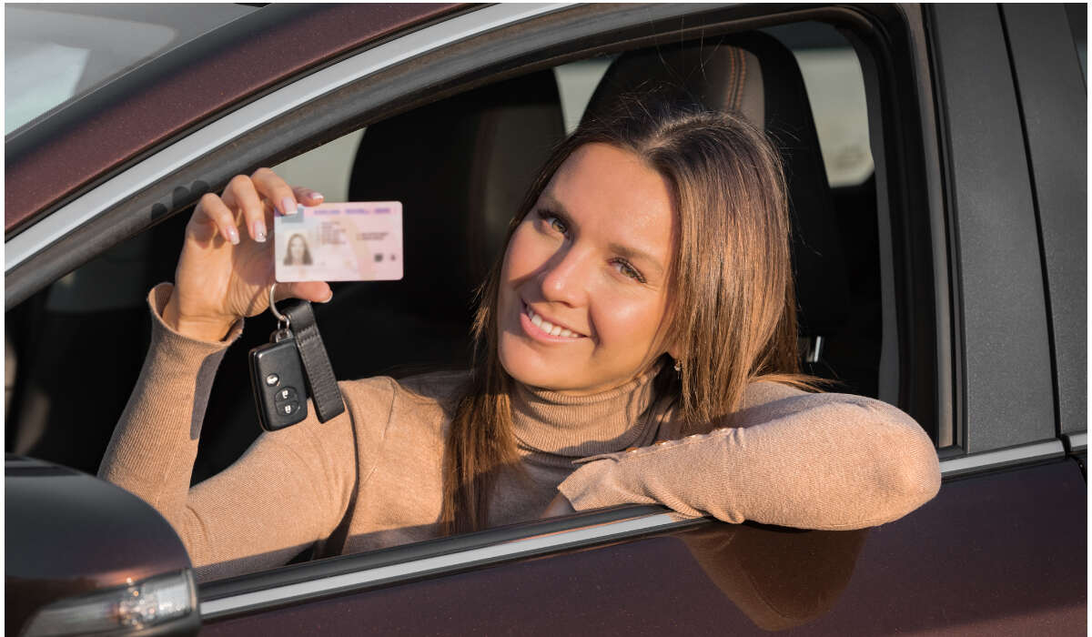 Ein Mädchen sitzt in einem Auto und hält ihren Führerschein in der Hand.-DE