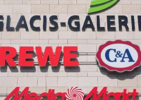 Große Schilder bekannter deutscher Geschäfte an einer weißen Wand